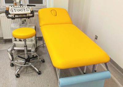 Żółta kozetka obok której stoi żółte krzesło obrotowe i sprzęt medyczny do USG.