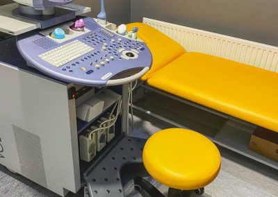 Żółta kozetka obok której stoi żółte krzesło obrotowe i sprzęt medyczny do USG.